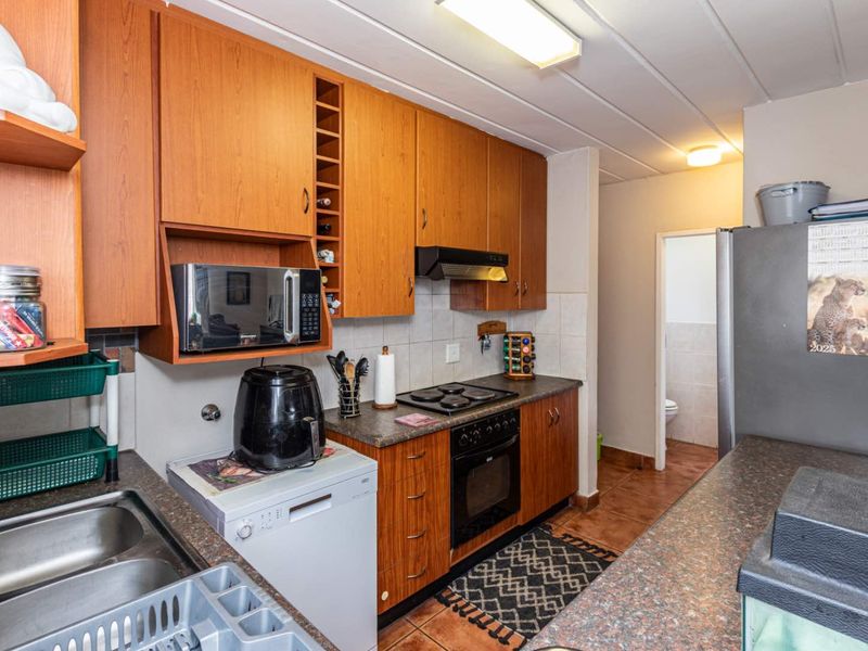 A functional kitchen featuring wood-look cabinetry, laminate countertops, built-in oven, electric hob, and a double bowl stainless steel sink with tiled flooring.