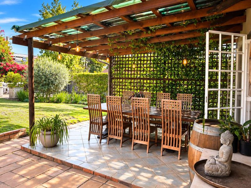 A charming covered patio area featuring a wooden pergola, tiled flooring, and lattice screening, providing a seamless transition to the lush garden.