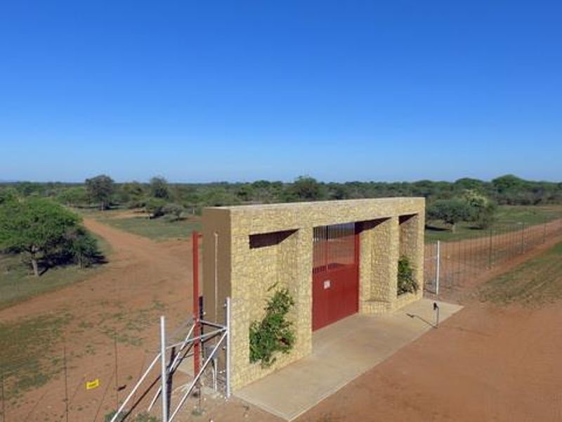 Aerial view of a secure farm entrance featuring a stone-clad gate structure, metal security gate, and extensive perimeter fencing on a rural property.