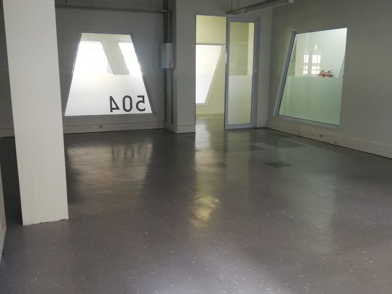 An empty, open-plan office space featuring exposed ceiling cable trays, vinyl flooring, and internal glass partitions with frosted detailing.