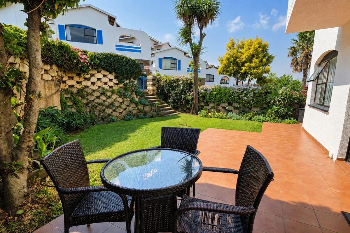 A private rear garden featuring a tiled patio area, established lawn, and a decorative stone retaining wall with integrated stairs.