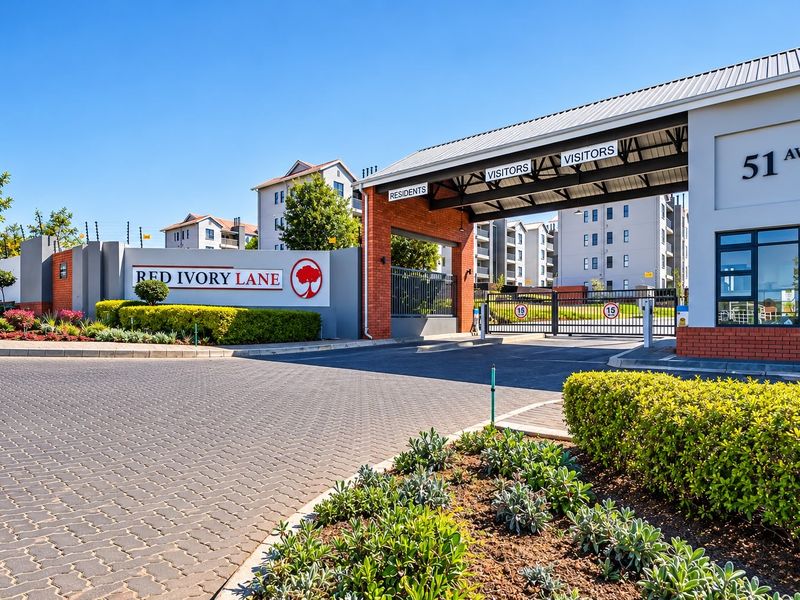 The secure entrance to Red Ivory Lane apartment complex, featuring a paved driveway, brick gatehouse, and well-maintained landscaped gardens.