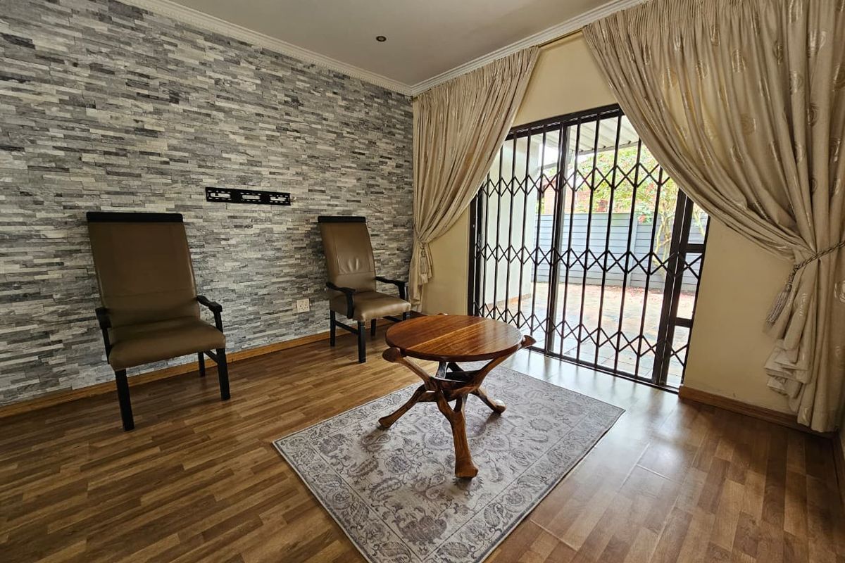 A living room featuring wood-look laminate flooring, a textured stone-cladding feature wall, and sliding glass doors with security gates leading to the exterior.