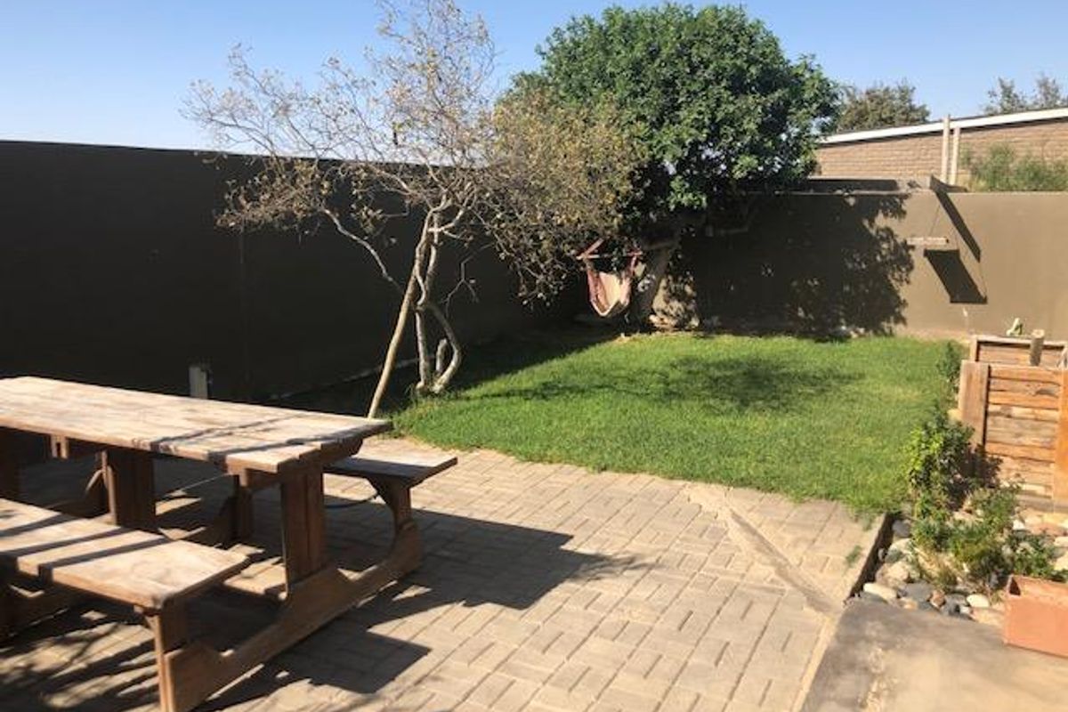 A private rear garden featuring a paved patio area, a small lawn, and high boundary walls for added privacy.