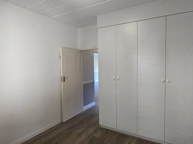 A clean, empty bedroom featuring built-in cupboards, modern laminate flooring, and a textured ceiling, offering a neutral canvas for personalization.