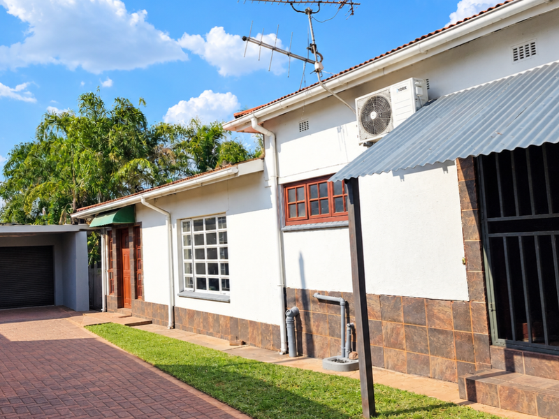 Front exterior view of the house featuring a paved driveway, garage, and tiled facade base with an installed air conditioning unit.