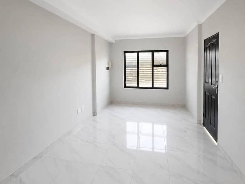 A bright, empty bedroom featuring modern white marble-look floor tiles, a black-framed window, and a contrasting black interior door.