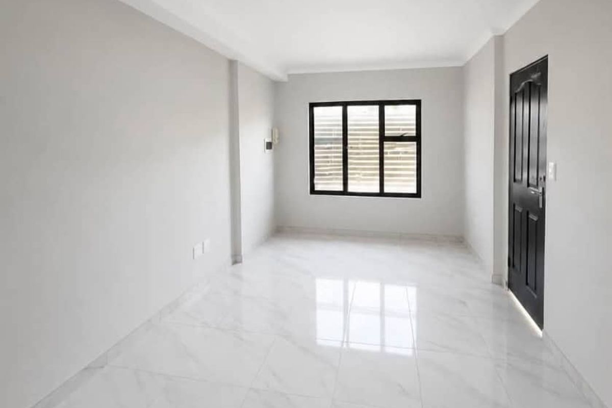 A bright, empty bedroom featuring modern white marble-look floor tiles, a black-framed window, and a contrasting black interior door.