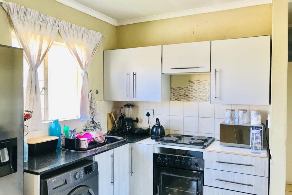 A functional kitchen featuring white cabinetry, granite countertops, a built-in oven with hob, and tiled backsplash, providing essential cooking and storage space.