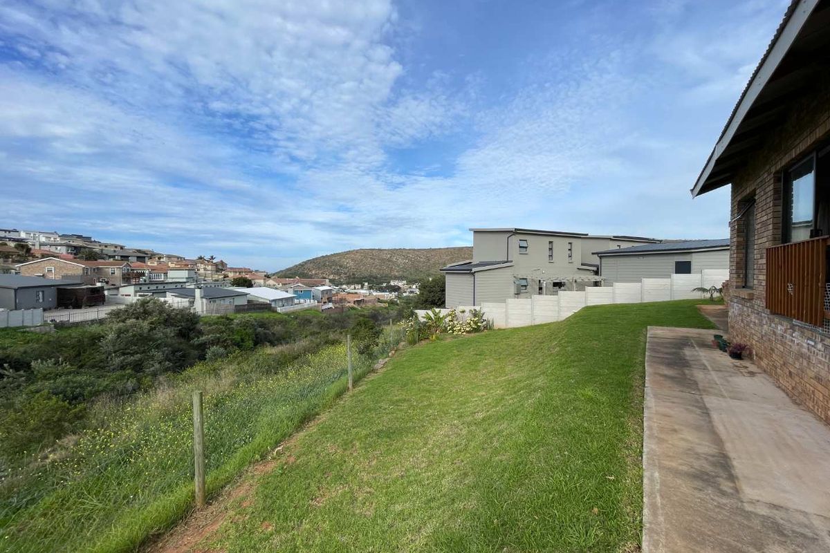 Rear view of the property featuring a lawn, concrete pathway, and brick exterior wall with views of the surrounding neighbourhood.