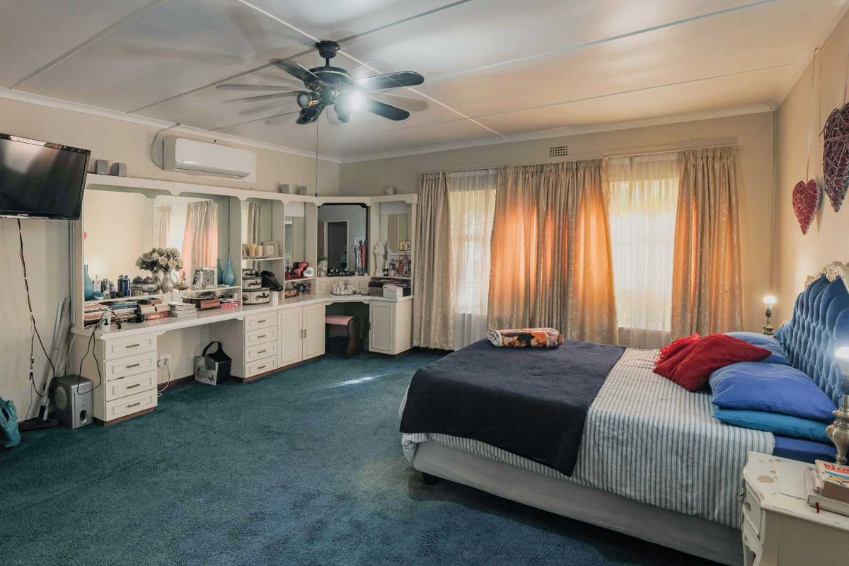 Spacious bedroom featuring built-in vanity cabinetry, ceiling fan, and wall-mounted air conditioning unit with large windows providing natural light.