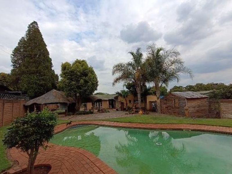 Outdoor pool area featuring a swimming pool, brick paving, a thatch lapa, and a wooden storage shed within a fenced garden setting.