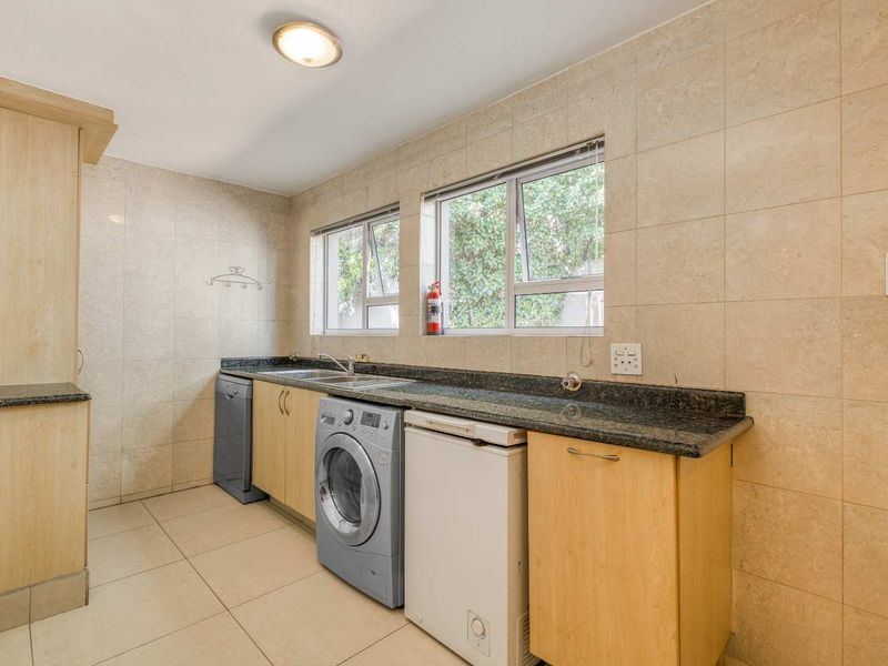 Functional laundry room featuring granite countertops, built-in cabinetry, double sink, and tiled finishes throughout.