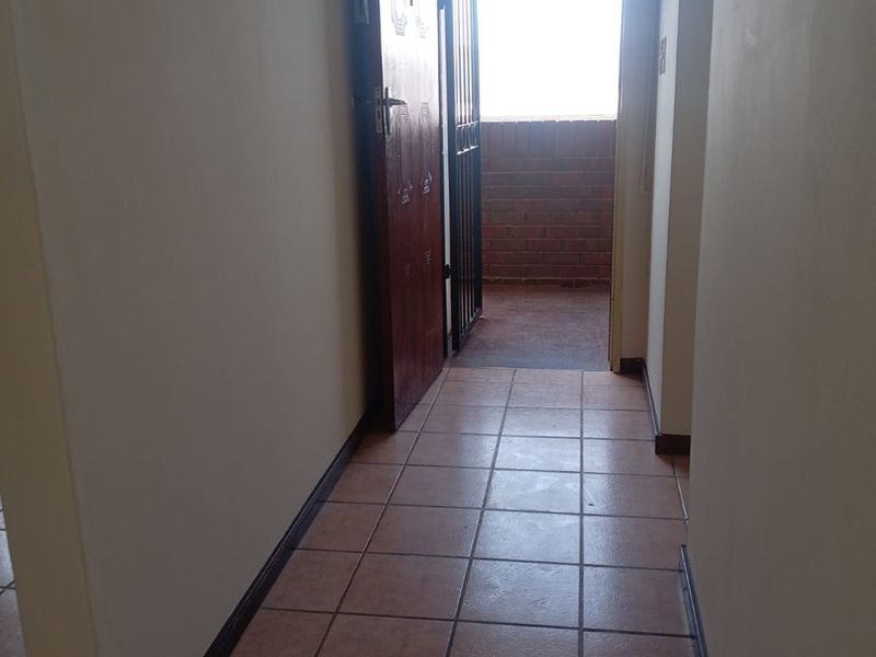 A functional hallway featuring tiled flooring and a security gate leading to an outdoor balcony area.