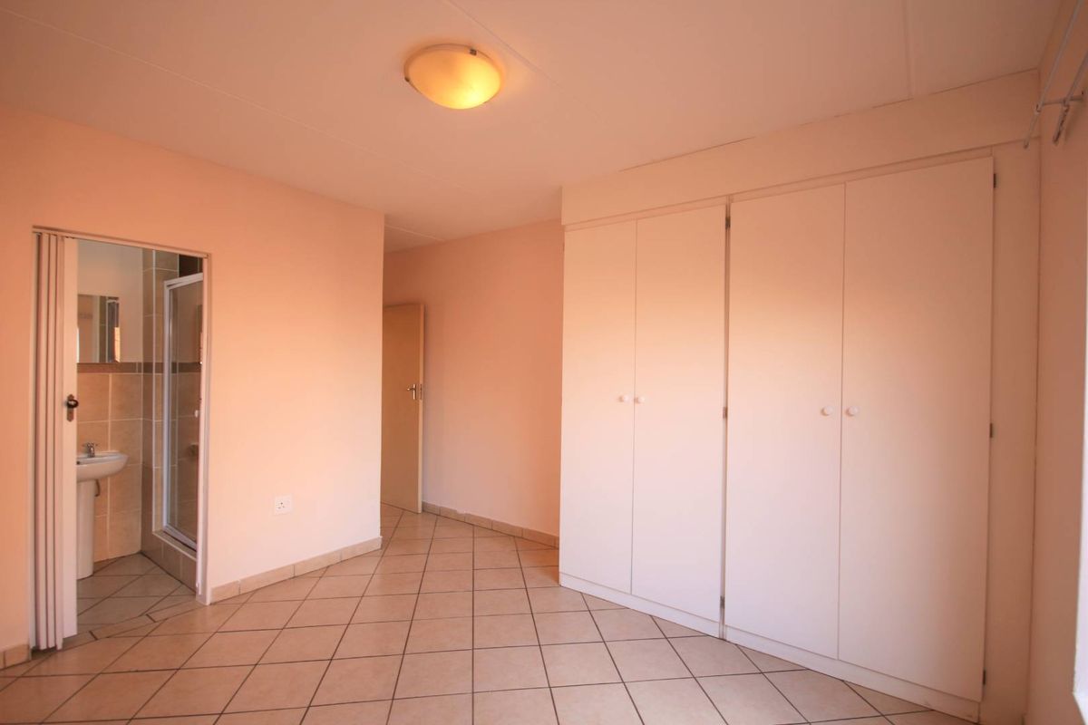 A spacious bedroom featuring neutral tiled flooring, ample built-in cupboard storage, and direct access to an en-suite bathroom.