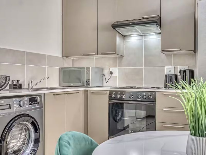 Modern kitchen featuring sleek cabinetry, tiled backsplash, built-in oven with hob, extractor fan, and an integrated washing machine.