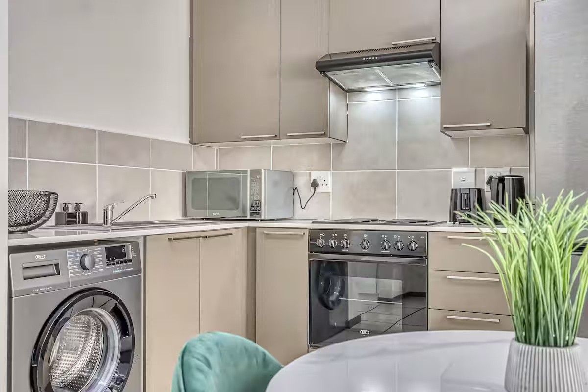 Modern kitchen featuring sleek cabinetry, tiled backsplash, built-in oven with hob, extractor fan, and an integrated washing machine.