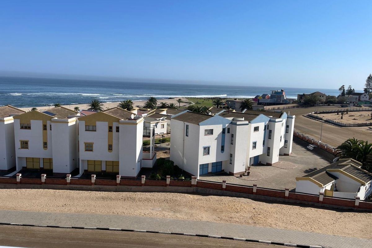 Elevated aerial view of the coastal residential complex, showcasing the building architecture, surrounding grounds, and proximity to the ocean.