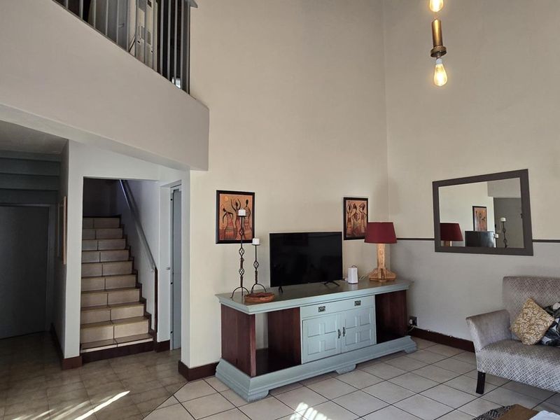Spacious double-volume living area featuring tiled flooring, a staircase leading to a mezzanine level, and neutral wall finishes.