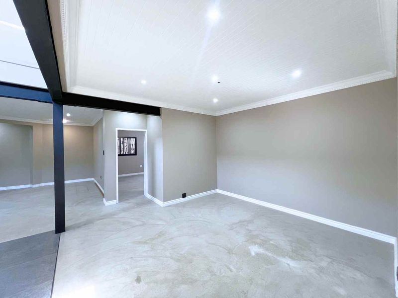 A spacious, empty living area featuring polished concrete floors, a modern exposed steel beam, and recessed ceiling lighting with neutral wall finishes.