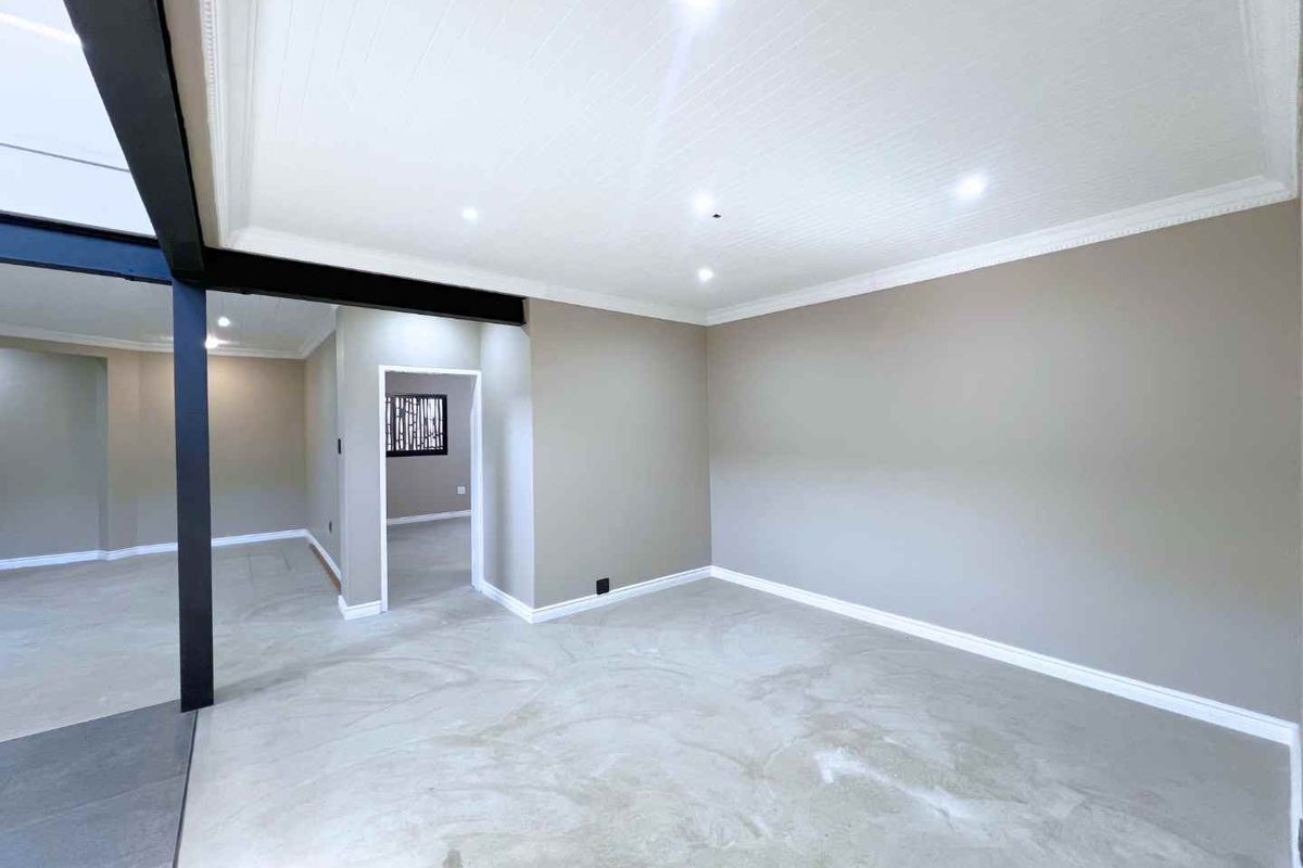 A spacious, empty living area featuring polished concrete floors, a modern exposed steel beam, and recessed ceiling lighting with neutral wall finishes.