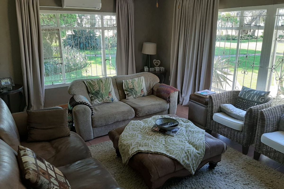 A comfortable living room featuring large windows with security bars, tiled flooring, and a wall-mounted air conditioning unit.