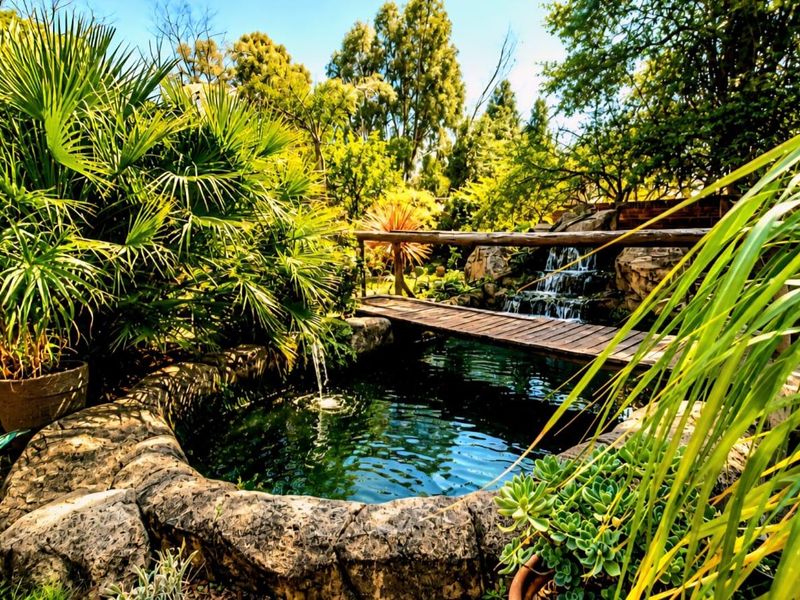 A beautifully landscaped garden featuring a stone-lined pond with a built-in water feature and a charming wooden footbridge.