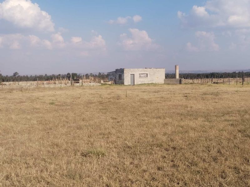 A wide view of a rural farm property featuring an unfinished concrete block structure and a silo set within a large open field.