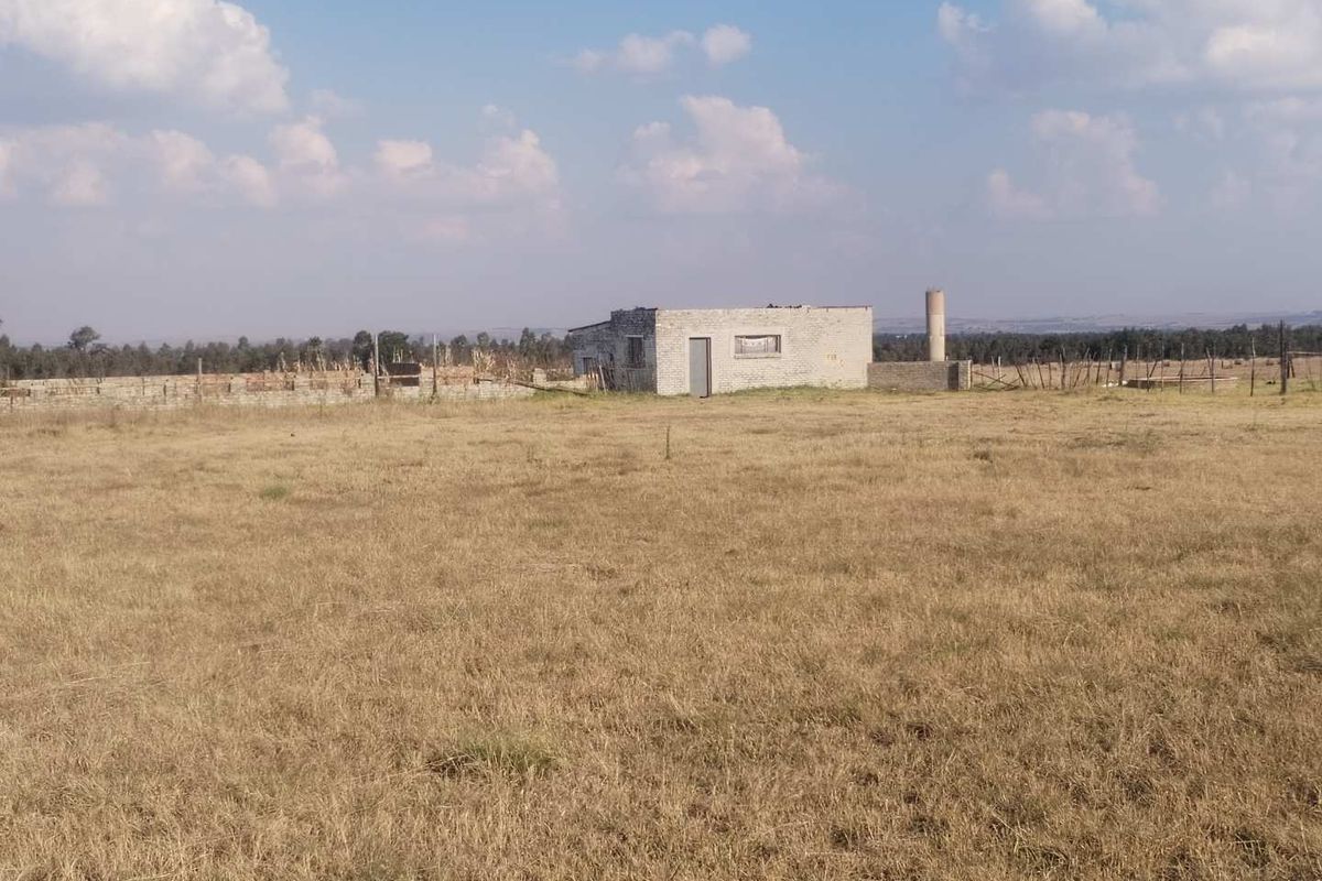 A wide view of a rural farm property featuring an unfinished concrete block structure and a silo set within a large open field.