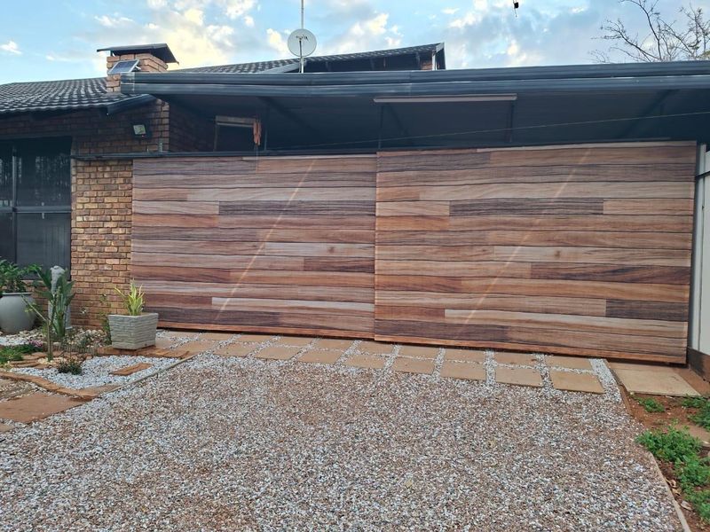 A residential garage featuring a modern wood-look sliding door, brick exterior, and a gravel driveway with paved walkway.
