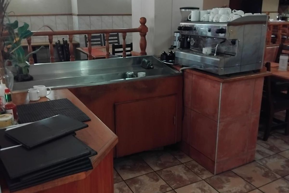 A commercial coffee preparation station featuring a built-in stainless steel sink, wooden cabinetry, and a professional espresso machine within a dining area.