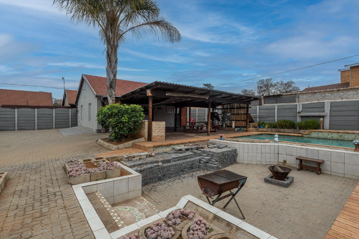 Rear exterior view featuring a swimming pool, covered patio area, paved courtyard, and secure boundary walling.