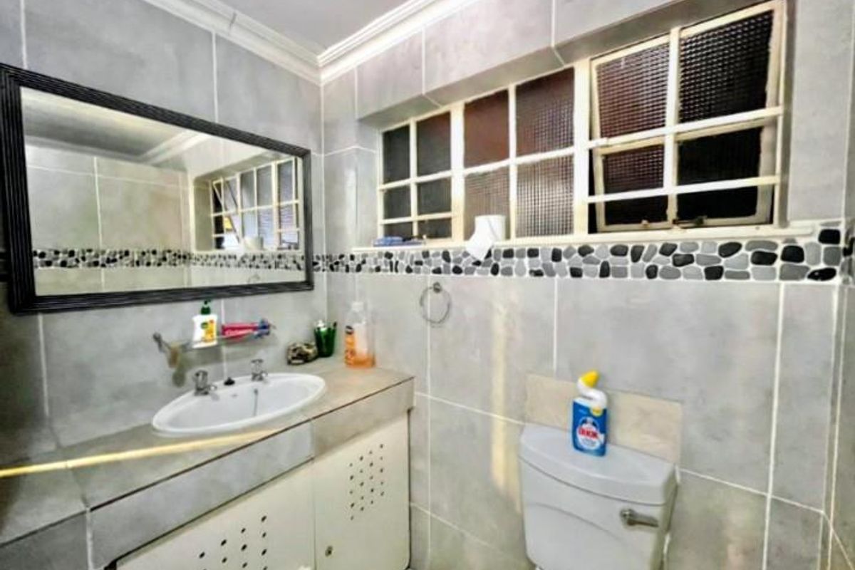A functional bathroom featuring a built-in vanity with integrated basin, wall-mounted mirror, and a standard toilet with tiled wall finishes.