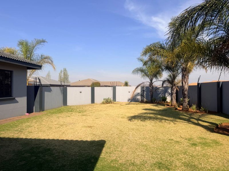A spacious rear garden featuring a well-maintained lawn, perimeter walling with integrated electric fencing, and established palm trees.