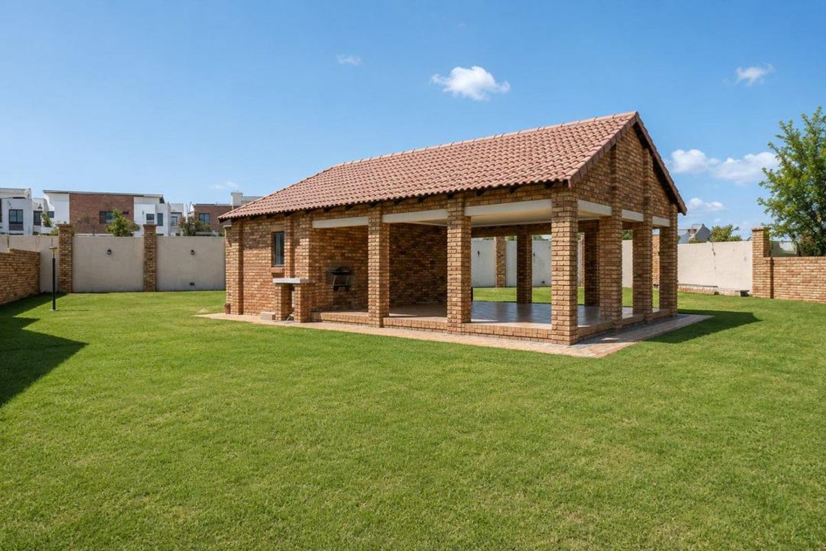 A spacious backyard featuring a well-maintained lawn and a large, covered brick lapa with a built-in braai, perfect for outdoor entertaining.