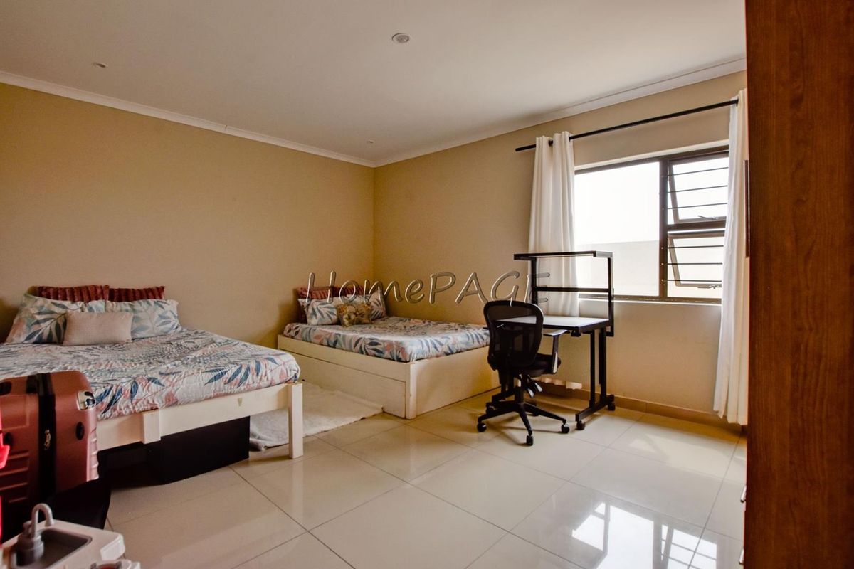Spacious bedroom featuring neutral wall tones, large format floor tiles, and natural light through an aluminium-framed window.