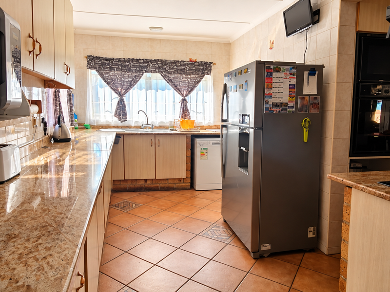 A functional kitchen featuring granite countertops, tiled flooring, built-in cabinetry, and integrated appliances including an oven and hob.