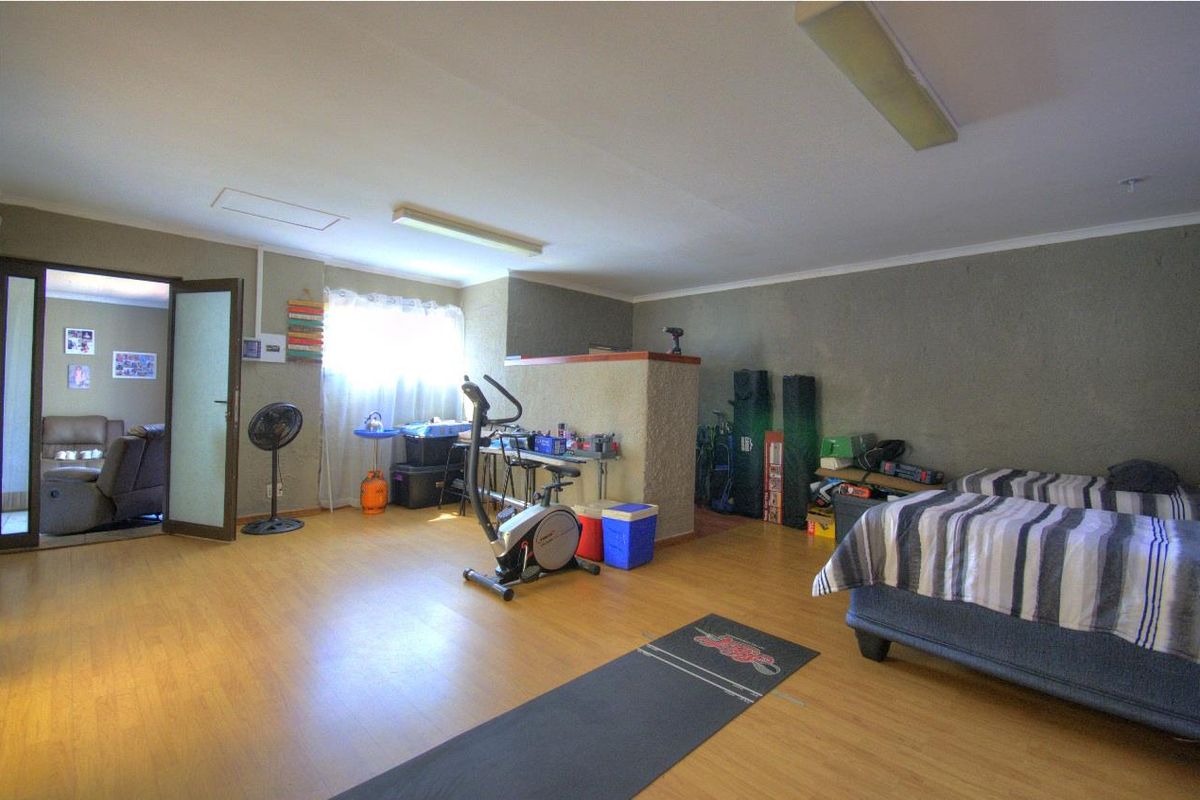 A multi-purpose room featuring laminate flooring, recessed lighting, and a partial partition wall, currently utilized as a bedroom and exercise space.