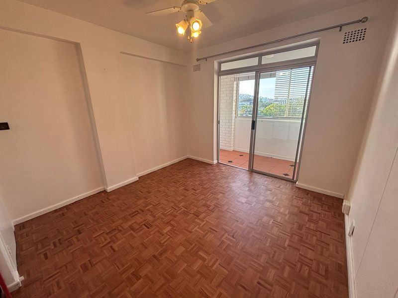 An empty bedroom featuring classic parquet flooring, a ceiling fan, and a sliding glass door providing access to an outdoor balcony area.