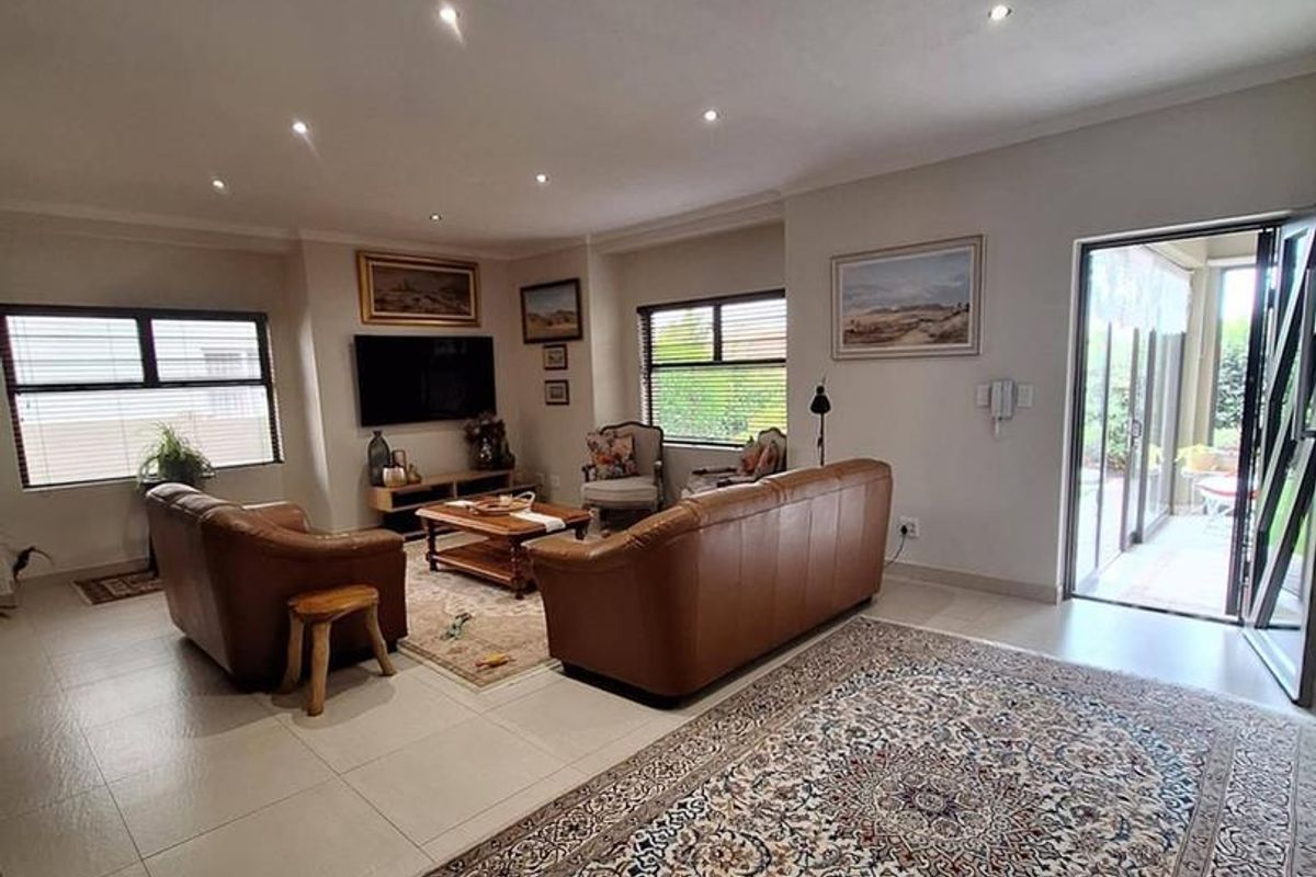 Spacious living room featuring neutral tiled flooring, recessed downlighting, and large sliding glass doors providing direct access to the outdoor patio area.