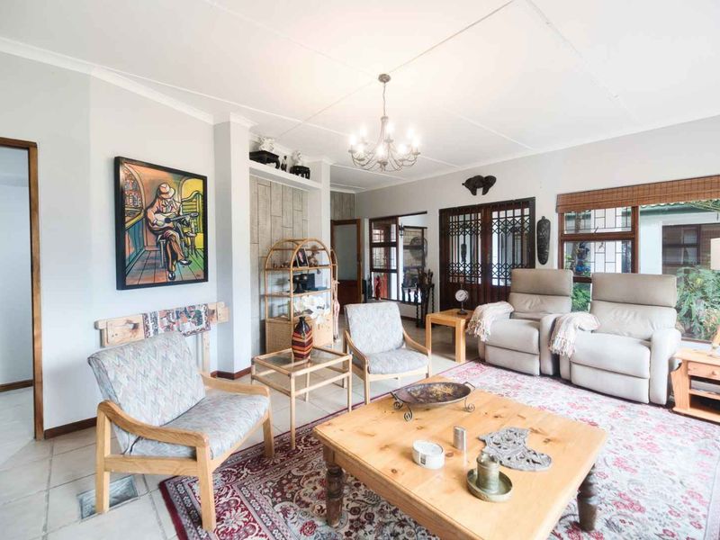 Spacious living room featuring tiled flooring, a central chandelier, and decorative stone wall accents, offering a comfortable and well-lit living space.