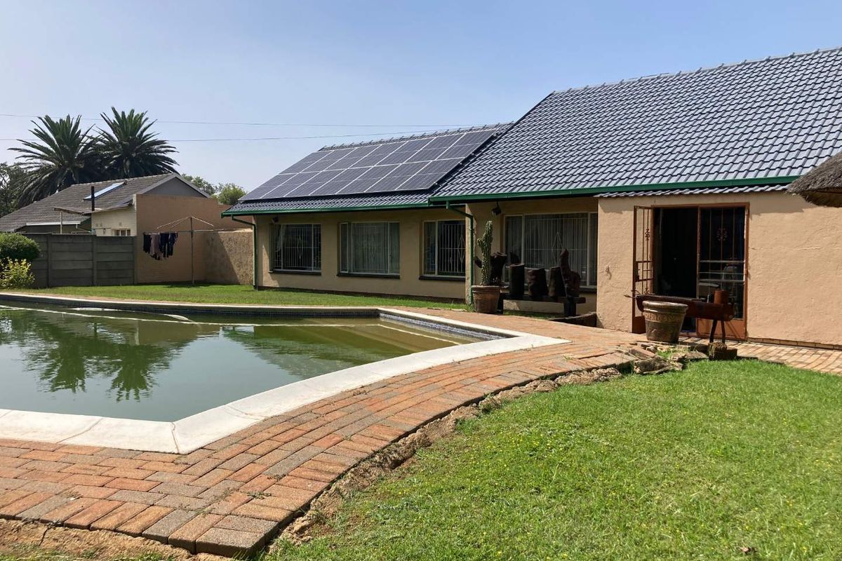 Rear view of the property featuring a swimming pool, brick paved patio area, and roof-mounted solar panels on a tiled roof.