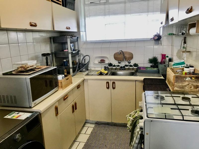 A compact kitchen featuring laminate countertops, tiled backsplash, built-in cabinetry, and a gas stove, offering a functional layout with potential for modernization.