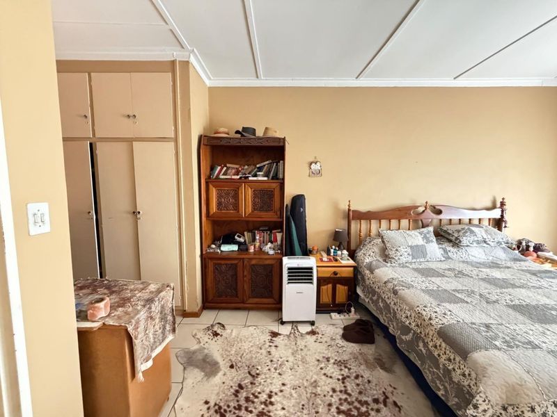 A bedroom featuring built-in cupboards, tiled flooring, and a panelled ceiling. The space requires cosmetic updates to improve its overall condition and appeal.
