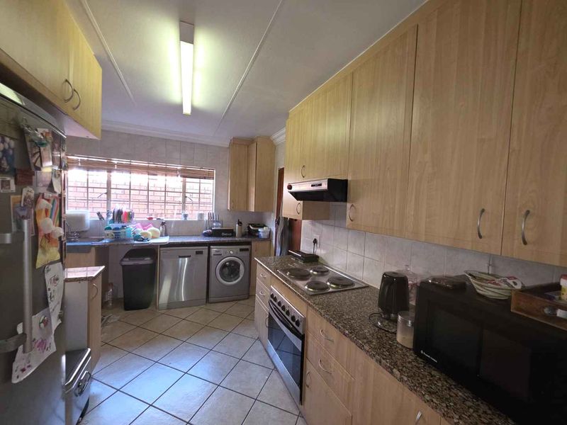 Functional kitchen featuring laminate cabinetry, granite countertops, built-in oven, electric hob, and tiled flooring with integrated laundry appliance space.
