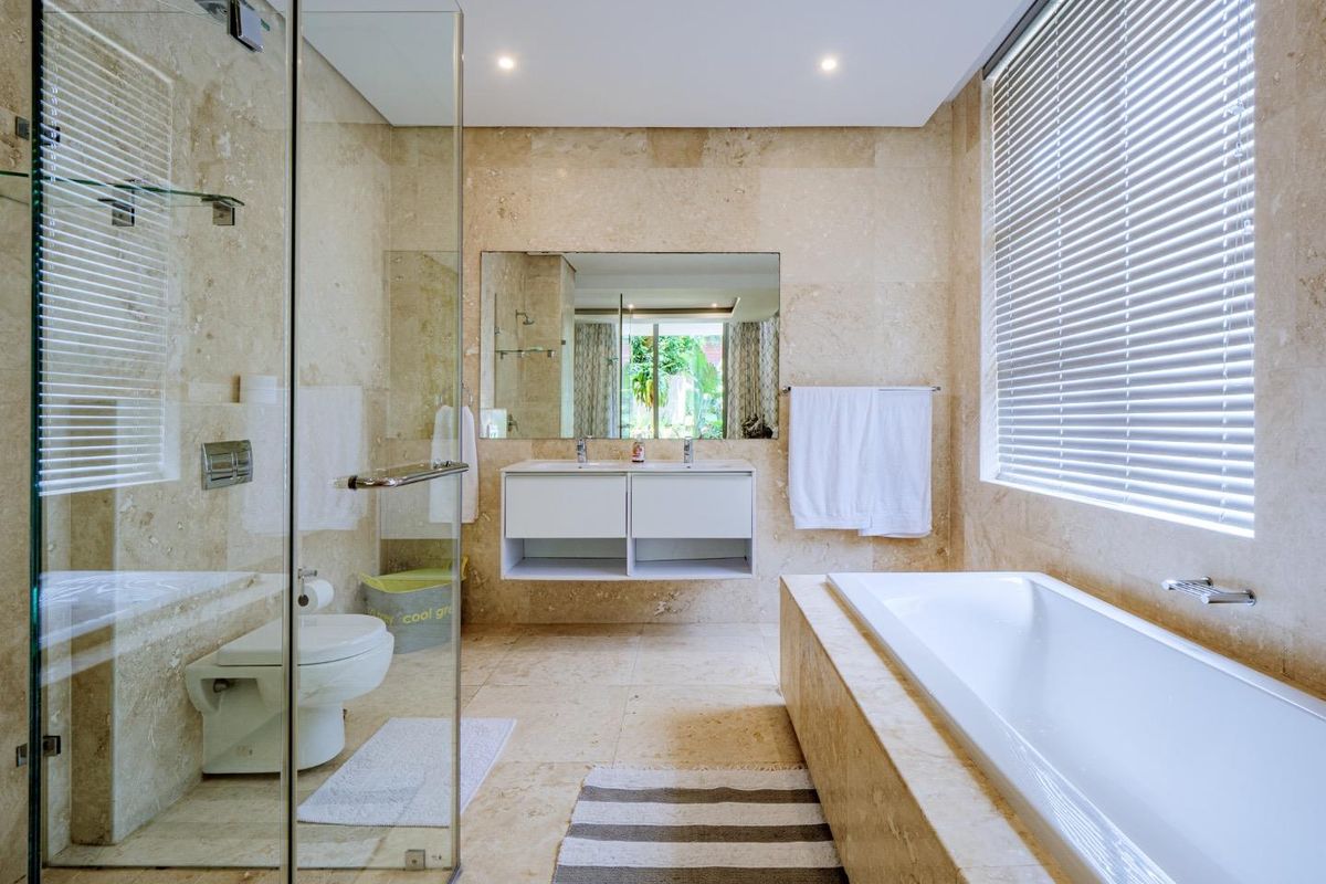 Modern bathroom featuring floor-to-ceiling travertine tiling, a floating double vanity, a glass-enclosed shower, and a built-in bathtub with natural light.