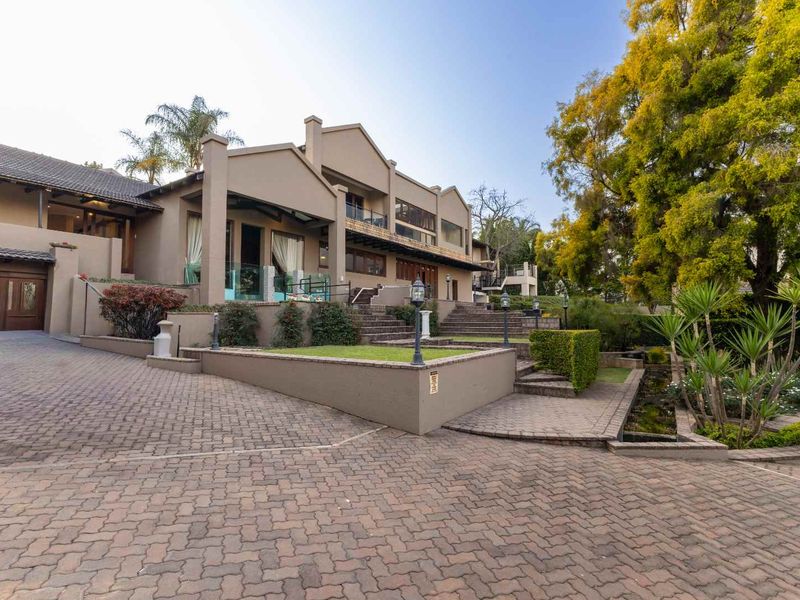 A well-maintained multi-level residential property featuring a paved driveway, landscaped garden, stone retaining walls, and an integrated garage.