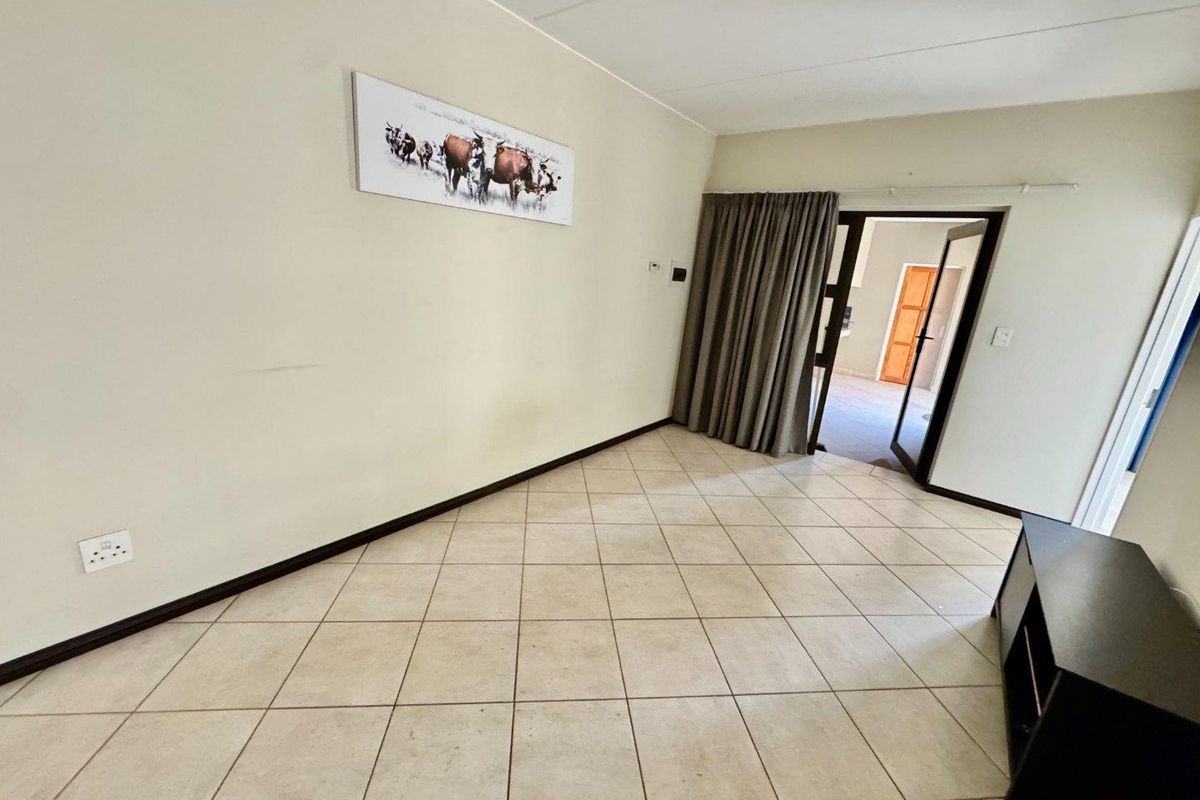 A living area featuring neutral tiled flooring and a doorway leading to an adjacent room, providing a functional and versatile space.