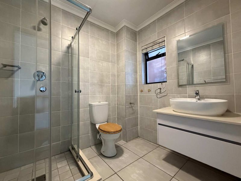 A modern, well-maintained bathroom featuring a glass-enclosed shower, a wall-mounted vanity with a vessel sink, and neutral floor-to-ceiling tiling.