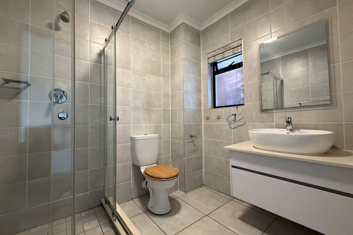 A modern, well-maintained bathroom featuring a glass-enclosed shower, a wall-mounted vanity with a vessel sink, and neutral floor-to-ceiling tiling.